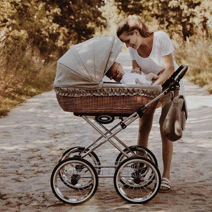 Mama pochylona nad niemowlęciem w eleganckim wiklinowym wózku retro, podkreślający komfort i bliskość.